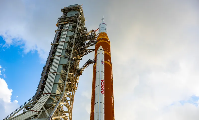 The SLS rocket and its launch tower under a cloudy sky