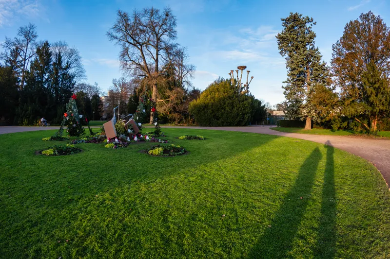 A park in Strasbourg with a lawn and bare trees under a blue sky