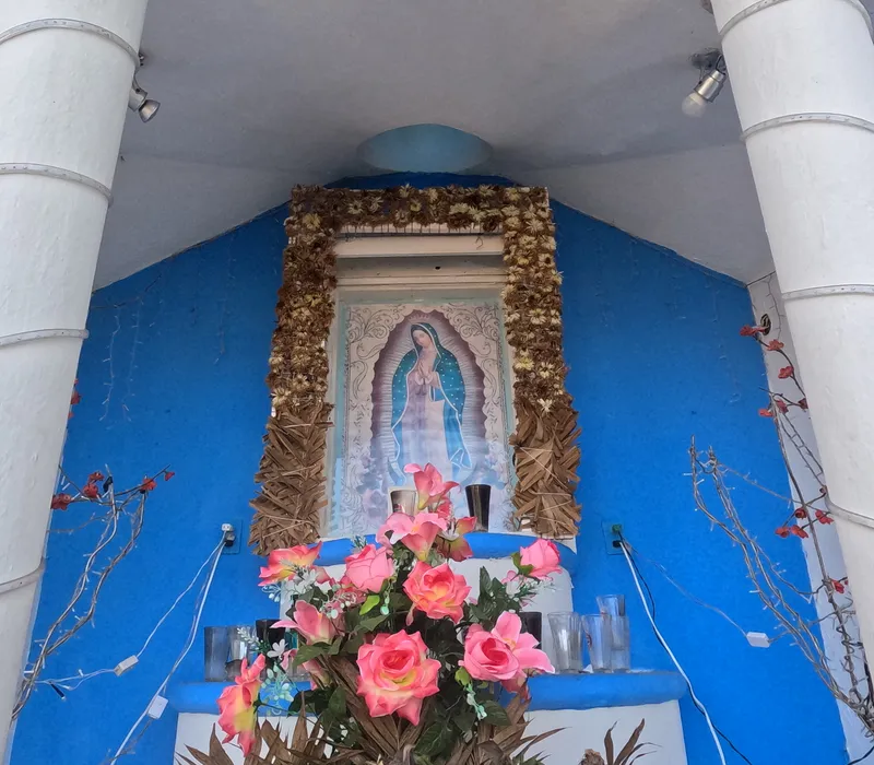 A shrine to the Virgin of Guadalupe with flowers in a blue chapel
