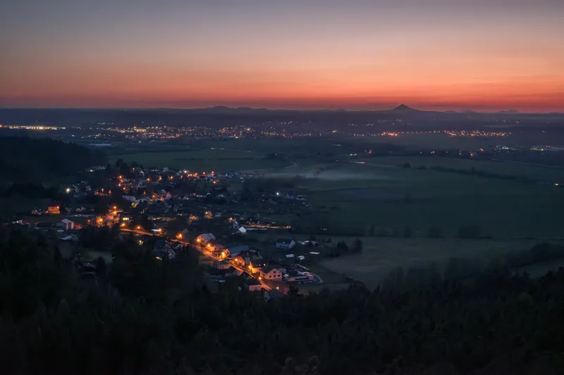 A valley with village lights below a red dusk sky in Bohemian Paradise