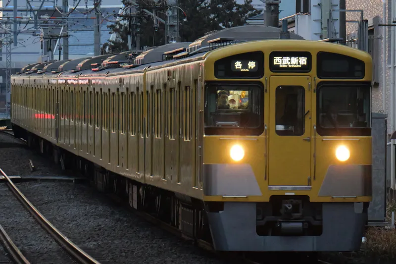 A yellow Seibu 2000 series train with its headlights on
