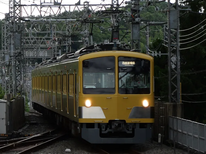 A yellow Seibu train running under overhead line masts