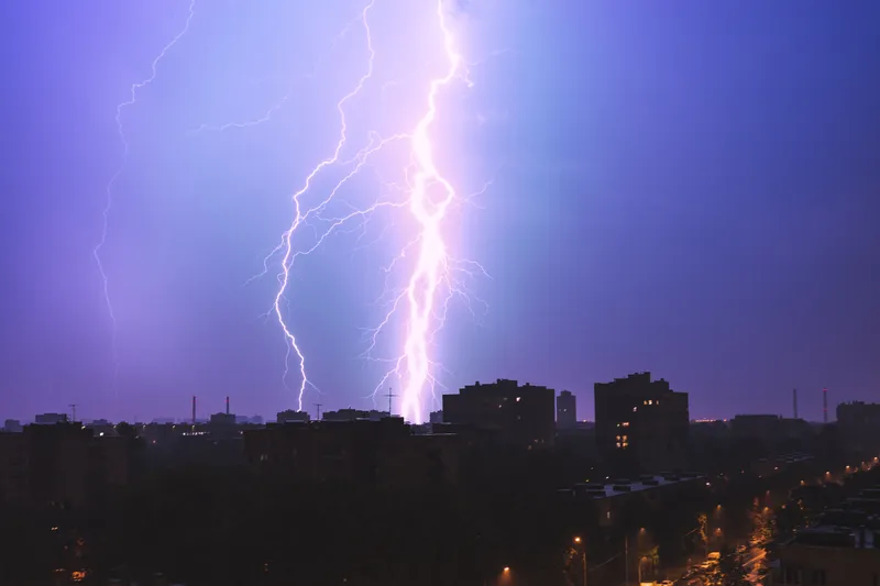 Lightning striking over city buildings at dusk