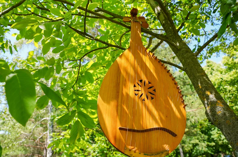 A wooden bandura hanging in a tree among green leaves